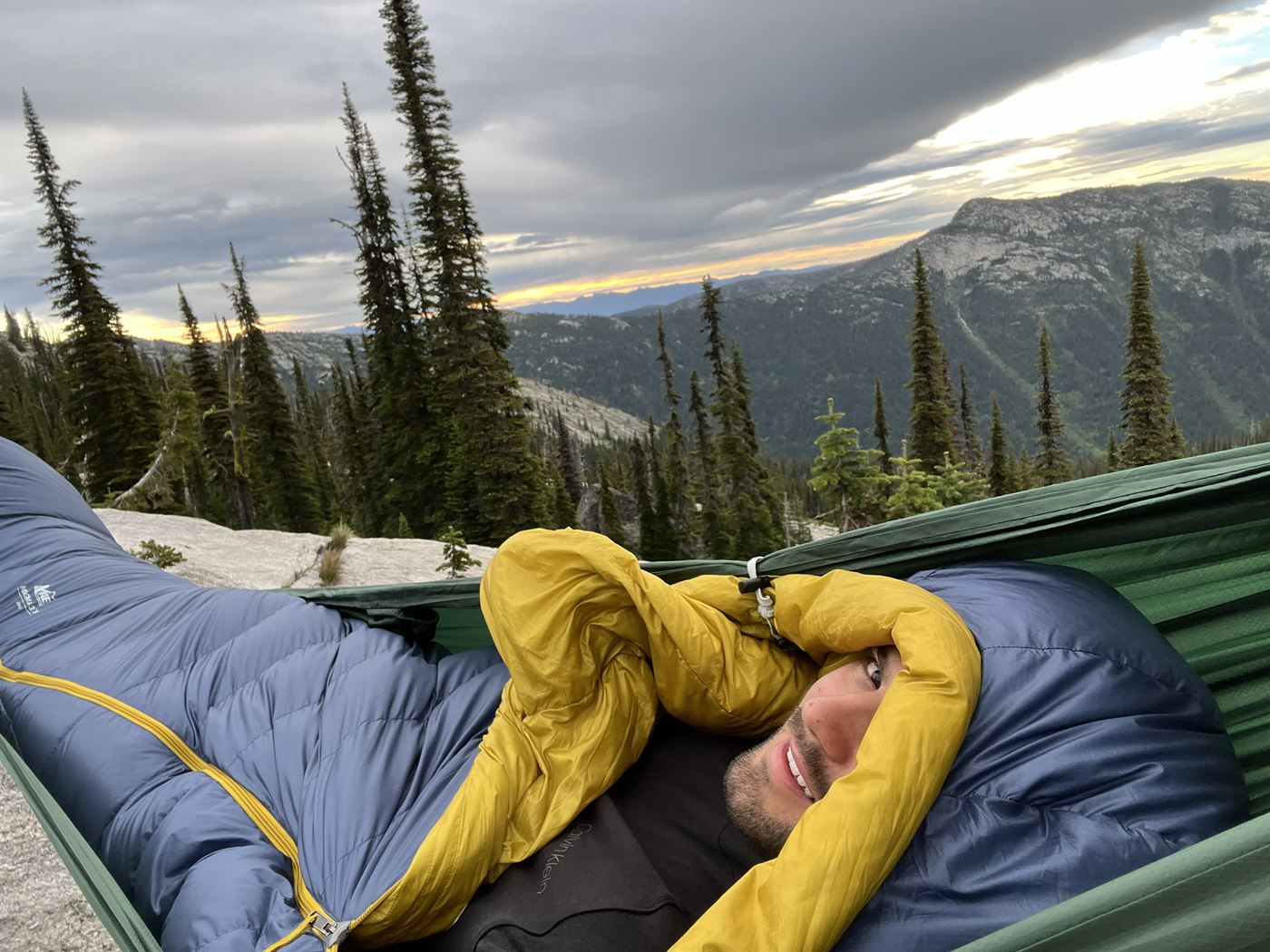 David in a sleeping bag at a backcountry campsite at sunset