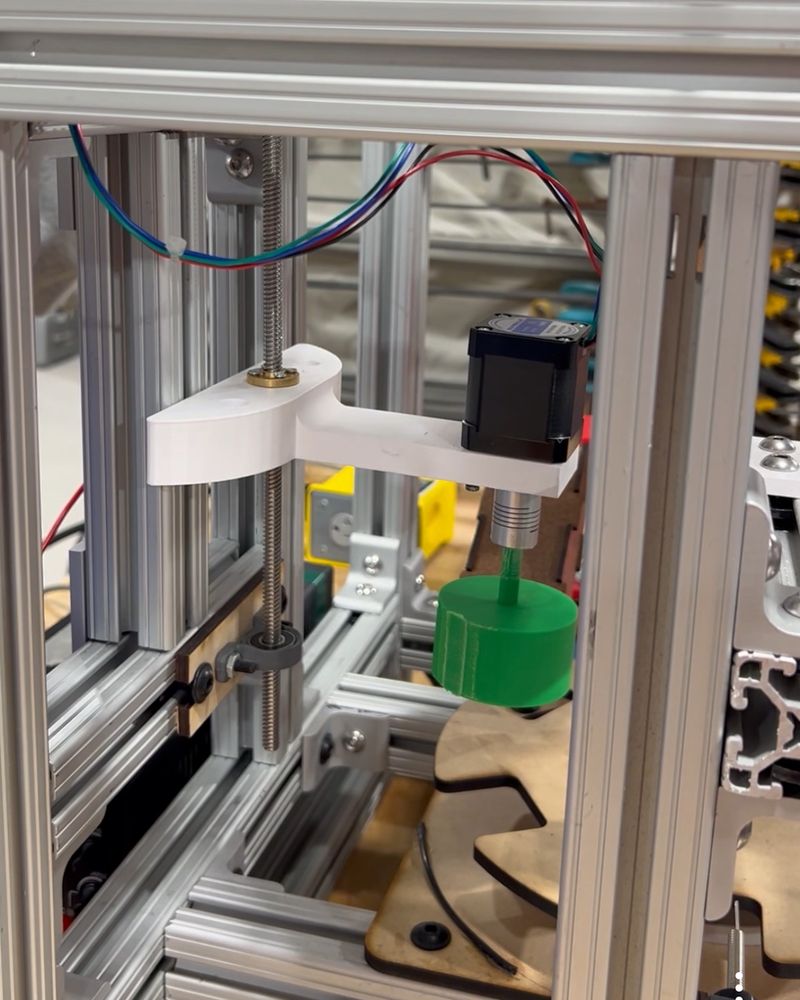 Capping head: a lead screw and stepper motor on a white printed bracket lower the green rubber-lined twister toward the rotary table